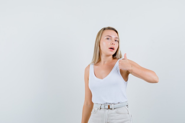 Dame blonde montrant le pouce en maillot, pantalon et à la fierté. vue de face.