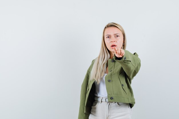 Dame blonde pointant la caméra en veste, pantalon et à la recherche de sérieux. vue de face.