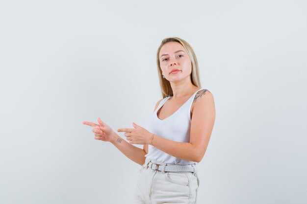 Dame blonde pointant de côté en maillot, pantalon et à la confiance, vue de face.