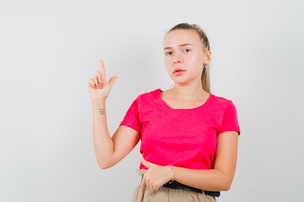 Dame blonde pointant les doigts de haut en bas en t-shirt rose, vue de face du pantalon.