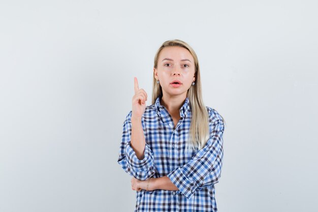 Dame blonde pointant vers le haut en chemise à carreaux et à la perplexité