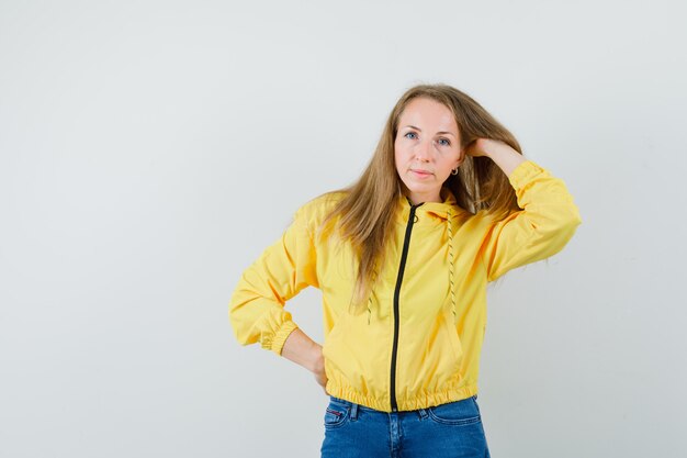 Dame blonde posant avec la main dans les cheveux en veste, jeans et jolie.