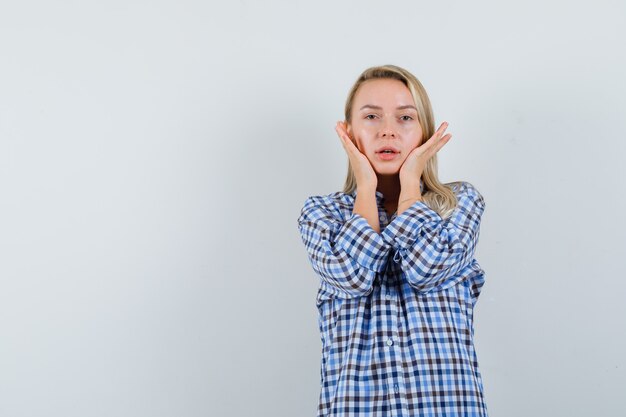 Dame blonde tenant les mains sur les joues en chemise décontractée et à la délicieuse