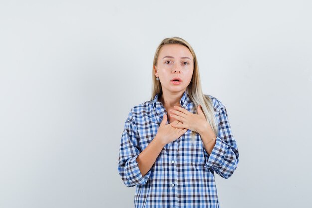 Dame blonde tenant les mains sur la poitrine en chemise à carreaux et à la perplexité