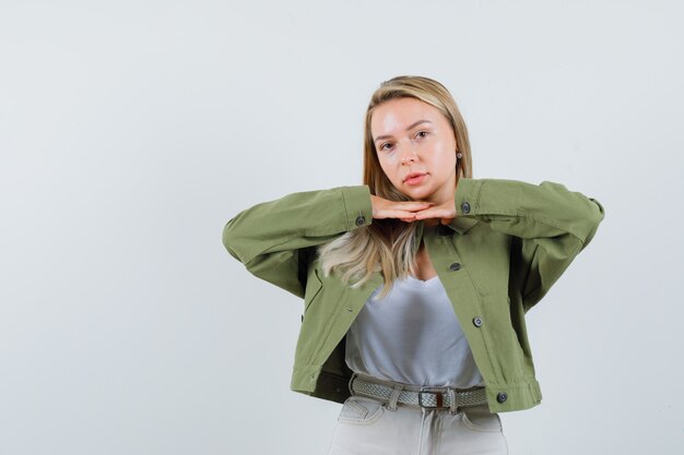 Dame blonde tenant les mains sous le menton en veste, pantalon et à la recherche de mignon. vue de face.