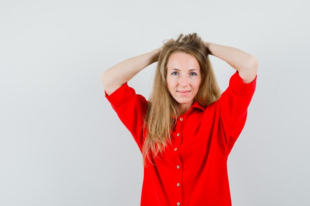 Dame blonde tenant les mains sur la tête en chemise rouge et à la recherche élégante.