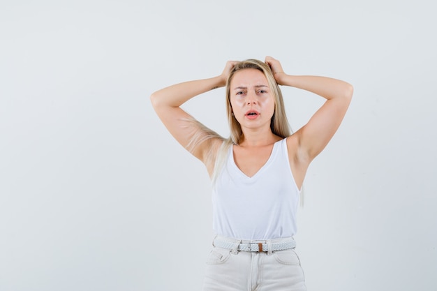 Dame blonde tenant les mains sur la tête en maillot, pantalon et à la triste