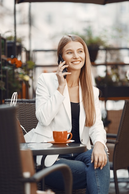 Dame boit un café. Femme assise à la table. Fille utilise un téléphone.