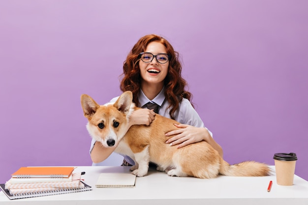 Dame bouclée en chemise et lunettes souriant et jouant avec corgi