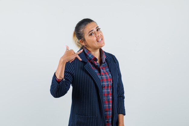 Dame en chemise, veste montrant le geste du téléphone et l'air confiant, vue de face.