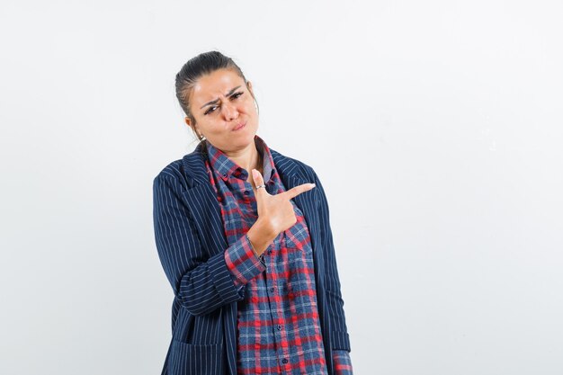 Dame en chemise, veste pointant vers le côté droit et regardant hésitante, vue de face.