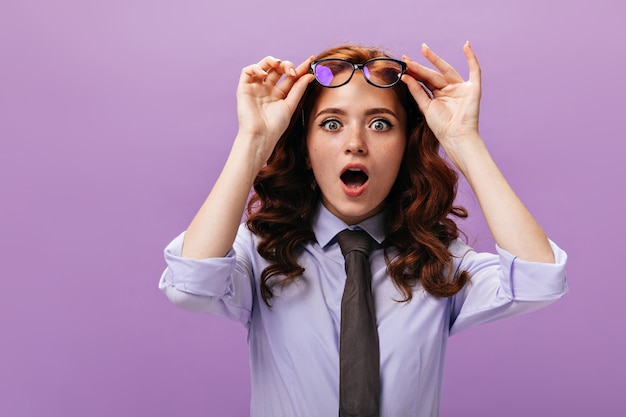 Une dame choquée enlève ses lunettes sur un mur violet