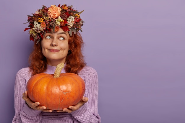 Dame de contenu pensif aux cheveux rouges tient une grosse citrouille mûre