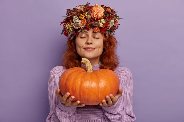 Dame de contenu pensif aux cheveux rouges tient une grosse citrouille mûre