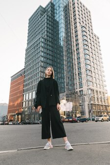 Dame élégante en vêtements sombres se dresse contre l'architecture moderne