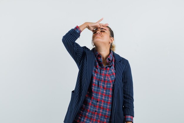 Dame frottant son front en chemise, veste et à la vue détendue, de face.