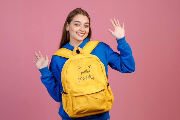 Dame joyeuse montrant des paumes tout en portant un drôle de sac à dos jaune devant elle en studio