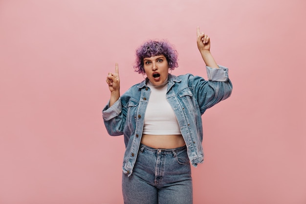 Photo gratuite dame à la mode effrayée avec une coupe de cheveux courte dans un pantalon serré. femme bouclée en t-shirt court posant sur rose.