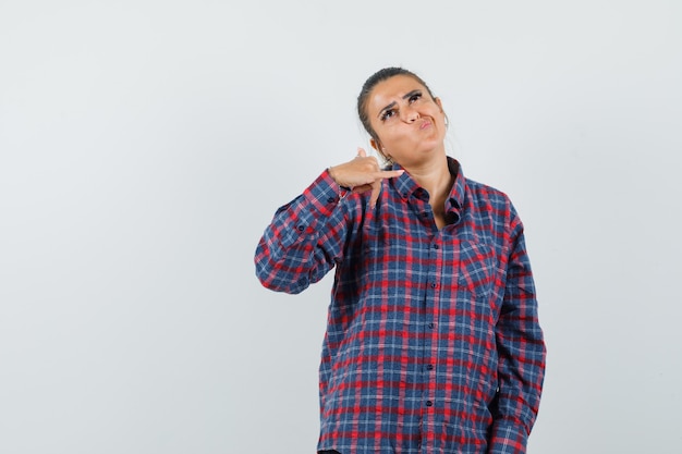 Dame montrant le geste du téléphone en chemise décontractée et à la recherche d'hésitant. vue de face.