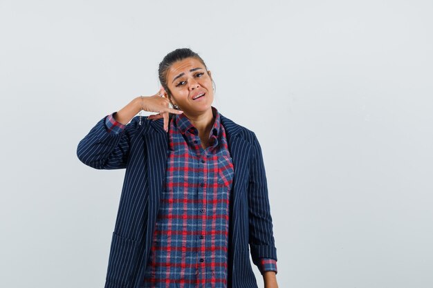 Dame montrant le geste du téléphone en chemise, veste et l'air inquiet. vue de face.