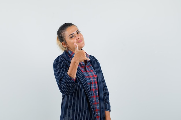 Dame montrant le pouce vers le haut en chemise, veste et à la vue confiante, de face.