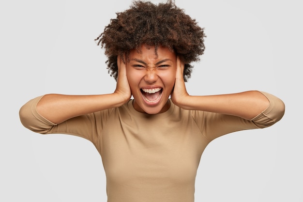 Une dame noire stressante et frustrée couvre les oreilles des deux mains, fronce les sourcils