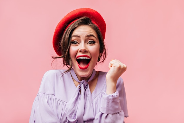 Photo gratuite dame optimiste en béret rouge et haut violet crie joyeusement sur fond rose.