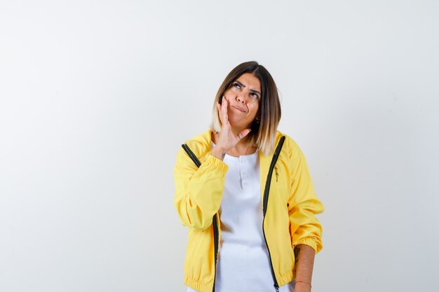 Dame penchée sur la joue en t-shirt, veste et regardant pensif, vue de face.