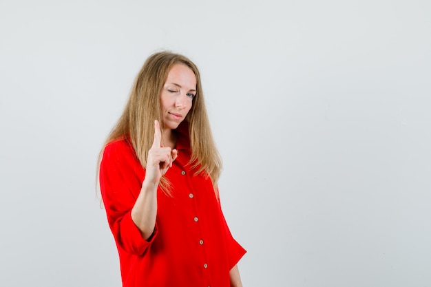 Dame pointant un œil en chemise rouge et l'air confiant.