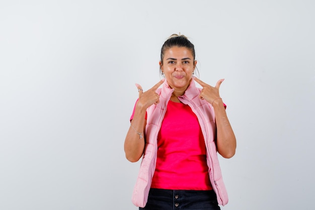 Dame pointant sur son visage en t-shirt, gilet et l'air confiant