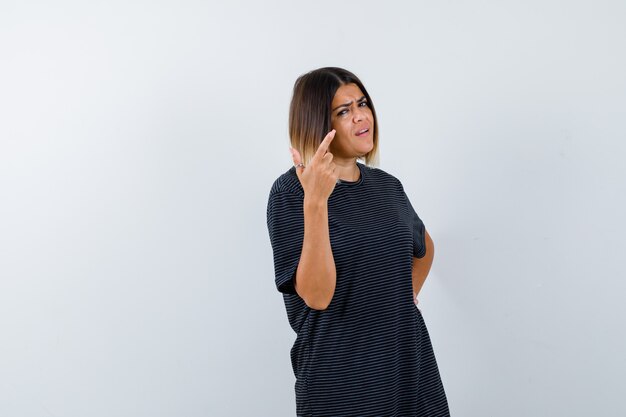 Dame pointant vers le coin supérieur droit en t-shirt noir et regardant hésitante, vue de face.