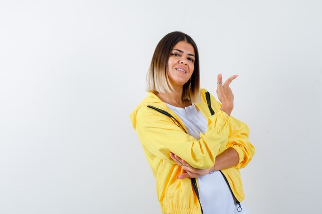 Dame pointant vers le coin supérieur droit en t-shirt, veste et regardant joyeux, vue de face.