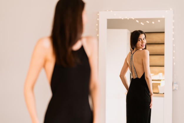 Photo gratuite dame porte une belle robe noire en regardant dans le miroir