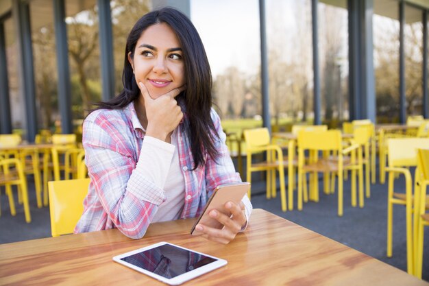 Dame positive à l&#39;aide de tablette et smartphone au café en plein air