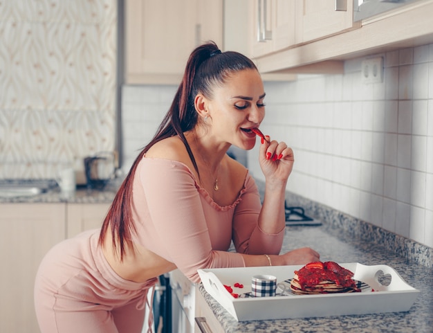 Dame séduisante dégustation de délicieux repas aux fraises dans la cuisine en haut rose et pantalon rose saumon