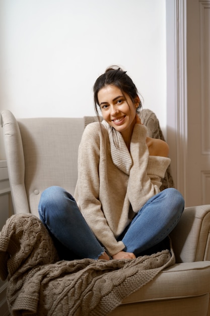 Dame souriante en vêtements à la mode intelligente est assise sur un fauteuil. Souriant, assis dans une atmosphère relaxante à l'intérieur