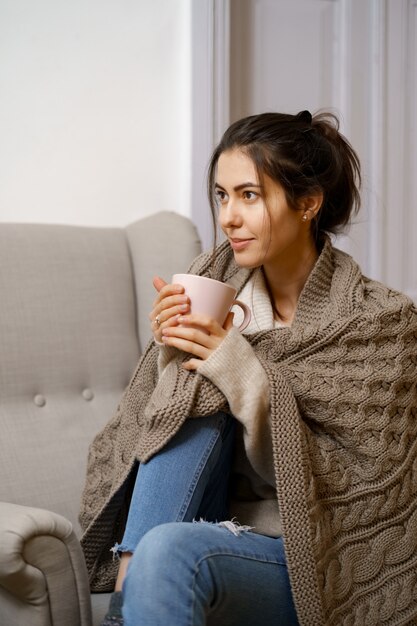 Dame souriante en vêtements à la mode intelligente est assise sur un fauteuil avec une tasse de thé.