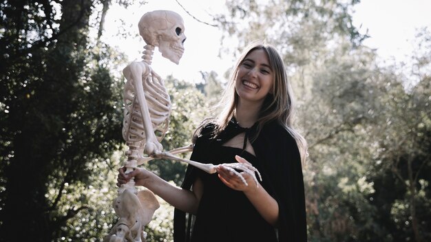 Dame souriante en vêtements de sorcière tenant le squelette