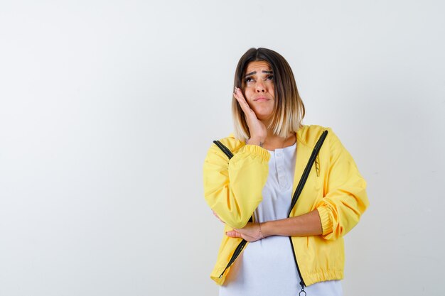 Dame en t-shirt, veste appuyée sur la joue sur la paume et à la rêveuse, vue de face.