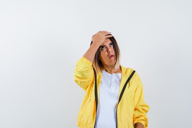 Dame en t-shirt, veste gardant la main sur la tête et l'air agacé, vue de face.