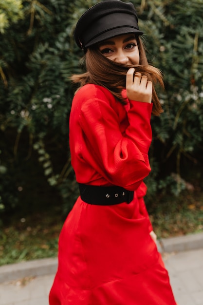 Photo gratuite une dame timide au regard sournois se promène dans le jardin botanique. portrait de jeune fille au chapeau en daim jouant avec ses cheveux