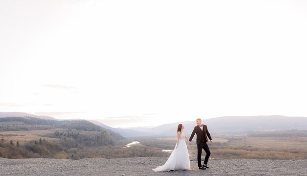 Dans le crépuscule avec un beau paysage, un couple de mariés se tient la main et se regarde