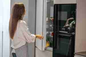 Photo gratuite dans la cuisine. jeune femme au foyer debout près du réfrigérateur dans la cuisine