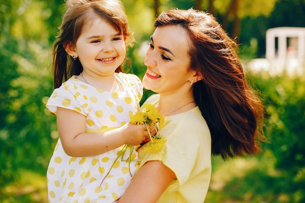 Dans Un Parc D'été Près D'arbres Verts, Maman Se Promène Dans Une Robe Jaune Et Sa Petite Fille Jolie