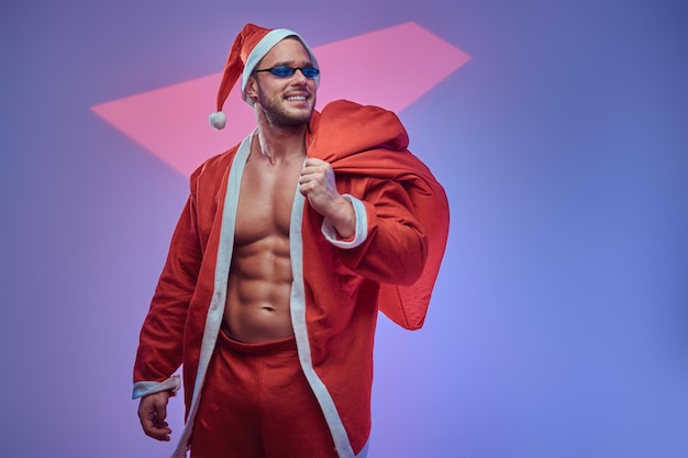 Dans le studio photo clair, un beau mec torse nu avec un sac de cadeaux pose pour le photographe.