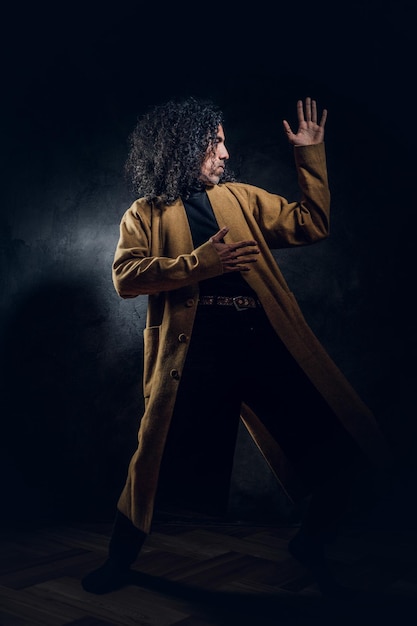 Dans un studio photo sombre, un homme élégant et charismatique pose pour le photographe.