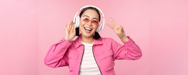 Danse élégante fille asiatique écoutant de la musique dans des écouteurs posant sur fond rose