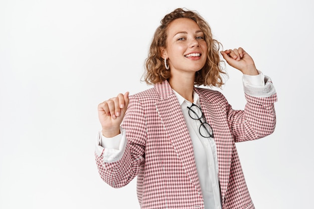 Photo gratuite danse femme entrepreneur souriante, s'amusant et se relaxant, debout en costume sur blanc. espace de copie