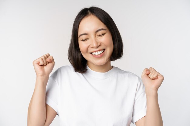 Danse fille asiatique célébrant le sentiment heureux et optimiste souriant largement debout sur fond blanc de studio