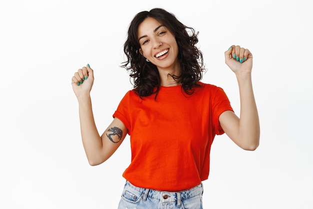 Danse queer girl riant, levant les mains et célébrant le concept lgbtq du mois de la fierté, s'amusant, debout sur blanc